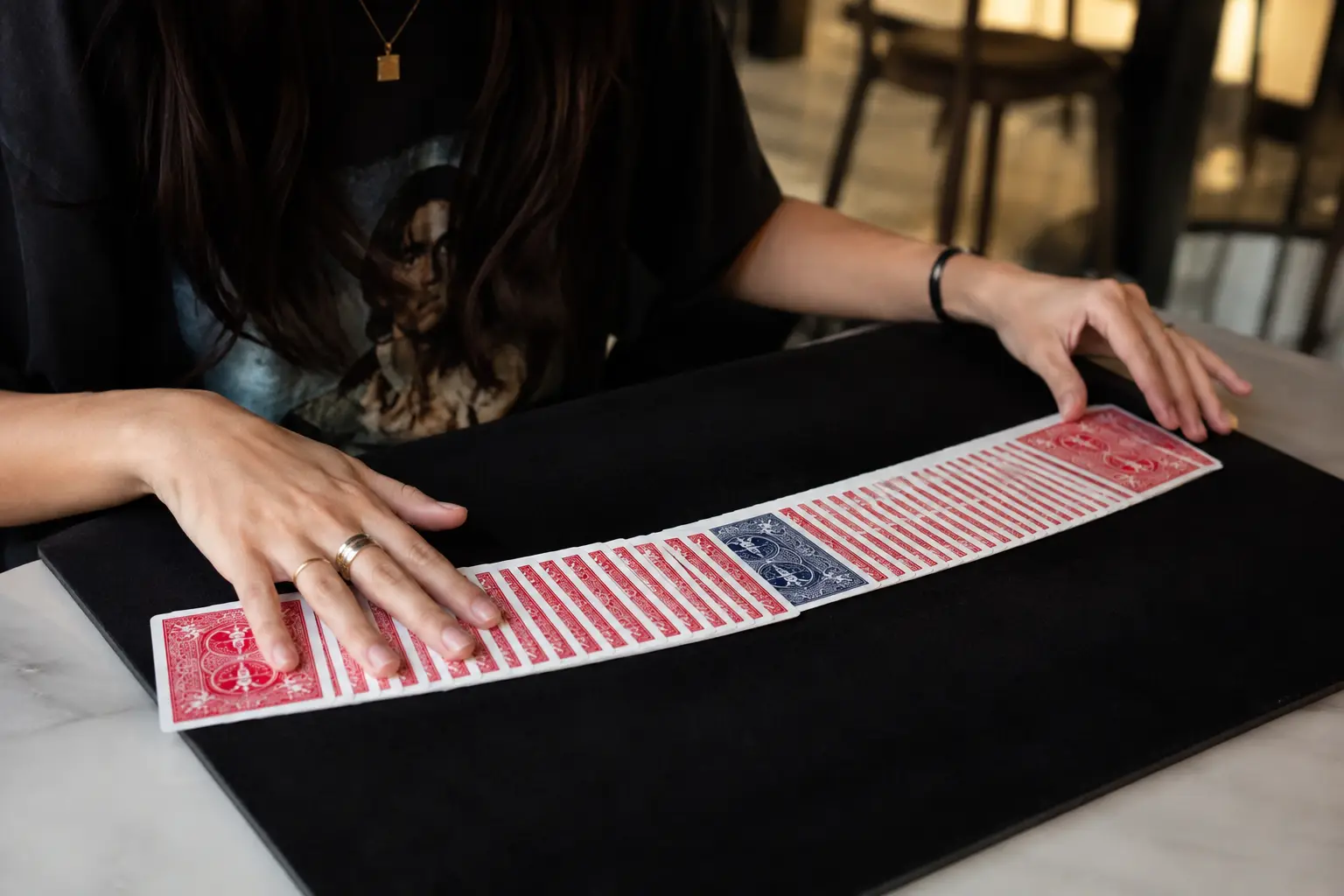 A magician's hands spread a ribbon of cards across a black close-up mat, one card reversed in the middle.